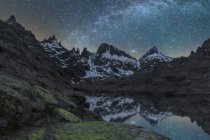 Pintoresca vista del cielo estrellado con galaxia reflejándose en el lago contra el monte con nieve al atardecer - foto de stock