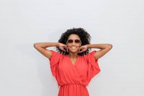 Trendige junge Afroamerikanerin mit lockigem Haar in roter Kleidung und Sonnenbrille blickt in die Kamera — Stockfoto