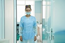 Alegre médico adulto femenino en máscara estéril y gorra ornamental mirando a la cámara en el hospital - foto de stock