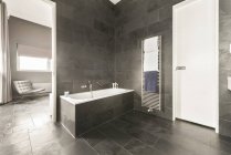 Interior do banheiro espaçoso com paredes de azulejos cinza e chão e banheira branca e pias — Fotografia de Stock