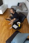 Von oben fokussierte erwachsene Männchen sitzen im Sessel neben Tisch mit einem Glas Orangensaft und verwenden Tablette am Morgen zu Hause — Stockfoto