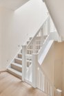 Intérieur de la maison moderne avec escalier menant à l'étage supérieur avec balustrade blanche et murs éclairés avec des lampes LED modernes dans le style loft minimaliste — Photo de stock