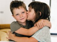 Conteúdo bonito gêmeos abraçando ternamente e beijando juntos na sala de estar em casa — Fotografia de Stock