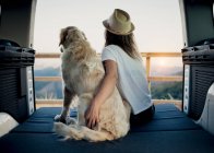 Irreconocible turista femenina abrazando obediente perro Golden Retriever acostado en el colchón dentro de autocaravana y admirando la naturaleza - foto de stock