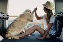 Loyal Golden Retriever dog giving high five to barefoot woman while sitting on bed inside RV during road trip in nature — Stock Photo