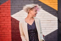 Безтурботний альтернативний жіночий кидання фарбованого короткого волосся на барвисту стіну в міській місцевості — стокове фото