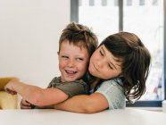 Carino contenuti gemelli abbracciano teneramente e seduti insieme in soggiorno a casa — Foto stock
