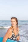 Donna in costume da bagno in piedi con tavola SUP in acqua di mare in estate e guardando altrove — Foto stock