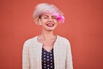 Carefree alternative female throwing dyed short hair against orange wall in urban area — Stock Photo