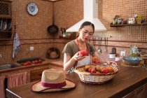 Femme au foyer ethnique ciblée sélectionnant des tomates fraîches sur la cuisine tout en cuisinant des aliments à la maison — Photo de stock