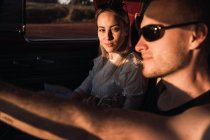 Side view of loving couple in sunglasses in vintage car while riding in nature in evening — Stock Photo