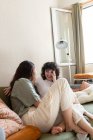 Восхитительные лесбиянки сидят вместе на диване в гостиной и смотрят друг на друга — стоковое фото