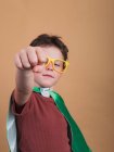 Niño en capa de superhéroe y gafas decorativas mostrando gesto de fuerza mientras mira a la cámara - foto de stock