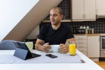 Konzentrierter Mann surft auf Tablet im Internet, während er zu Hause am Tisch sitzt und morgens frühstückt — Stockfoto