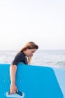 Вид сбоку женщины в купальнике, стоящей с доской SUP в морской воде летом и отводящей взгляд — стоковое фото