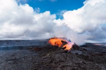 Vista pitoresca de Fagradalsfjall com fogo rápido e lava sob fumaça difusa em montanhas com nuvens fofas na Islândia — Fotografia de Stock