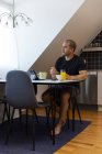 Focused male surfing Internet on tablet while sitting at table at home and enjoying breakfast in morning looking away — Stock Photo