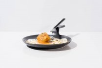 Metal fork with fresh piece of bread dipped in liquid yolk of fried egg served on skillet on white background — Stock Photo