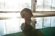 Junge schöne Frau am Bordstein des Hallenbades, mit schwarzem Badeanzug, Sonnenstrahlen, die durch das Fenster eintreten — Stockfoto