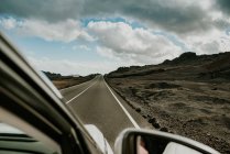 Véhicule conduisant sur route asphaltée à travers un terrain volcanique aride par temps couvert dans la nature de Fuerteventura, Espagne — Photo de stock