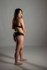 Confident Asian female in black lingerie standing on gray background in studio and looking at camera — Stock Photo