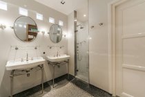 Elegante diseño interior de la casa de amplio baño blanco claro con espejos sobre lavabos dobles en apartamento contemporáneo - foto de stock