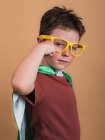 Side view of child in superhero cape and decorative glasses showing strength gesture while looking at camera — Stock Photo