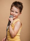Bambino fresco nel cantare in microfono moderno su sfondo marrone in studio — Foto stock