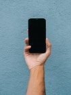 Ernte unkenntlich männlich zeigt moderne Handy mit schwarzem Bildschirm auf blauem Hintergrund in der Stadt — Stockfoto