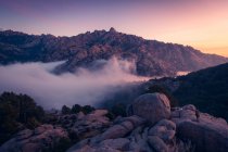 Сценічний вигляд Педрізи з туманом, який дифундує між горами Гвадарама та валунами з хвойними деревами на світанку в Іспанії. — стокове фото