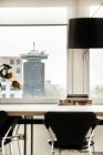Интерьер современной квартиры со столом и стульями расположен возле панорамного окна с видом на городской пейзаж с современной архитектурой при дневном свете — стоковое фото