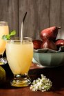 Copos de deliciosas bebidas refrescantes com suco de pêra e folhas de sabugueiro frescas na mesa — Fotografia de Stock