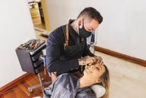 De cima homem em máscara manchando fundação de cara de mulher loira durante o trabalho em estúdio de maquilagem profissional — Fotografia de Stock