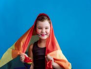 Menina sorridente com bochecha pintada com bandeira multicolorida em fundo azul vívido — Fotografia de Stock