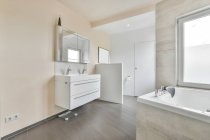 Intérieur de salle de bain spacieuse avec des murs beige clair meublés avec double lavabo sous miroir et baignoire dans un appartement moderne — Photo de stock