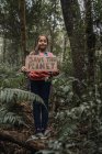 Niño étnico criando una pieza de cartón con la inscripción Save The Planet mientras mira la cámara en el bosque verde - foto de stock