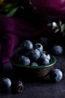 Closeup of pile of ripe blueberries in bowl served on black table with purple cloth — Stock Photo