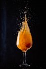 Холодный алкоголь апельсиновый напиток выплескивается из стеклянного кубка на черном фоне в студии — стоковое фото