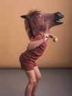 Вид сбоку анонимного ребенка в маске лошади наклоняется вперед, представляя концепцию скачущего жеребца на бежевом фоне — стоковое фото