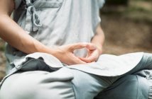 Cropped unrecognizable man in traditional clothes sitting on rock in Lotus pose and meditating during kung fu training in forest — Stock Photo