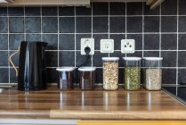 Recipientes de plástico com muesli e sementes de girassol e abóbora colocados perto de grãos de café e chaleira elétrica no balcão na cozinha — Fotografia de Stock