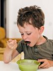 Adorabile ragazzo mangiare zuppa di panna appetitosa con cucchiaio durante il pranzo a casa — Foto stock
