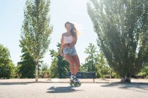 Знизу молода жінка в роликових лопатях показує трюк на дорозі в місті влітку дивлячись на камеру — стокове фото