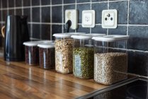 Plastikbehälter mit Müsli und Sonnenblumen- und Kürbiskernen in der Nähe von Kaffeebohnen und Wasserkocher auf der Theke in der Küche — Stockfoto