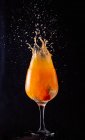 Bebida de laranja com álcool frio salpicando de cálice de vidro no fundo preto no estúdio — Fotografia de Stock