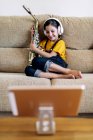 Niño consciente en auriculares y saxofón en la grabación del sofá en casa - foto de stock
