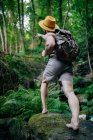 Von unten ein hirnloser Mann mit Rucksack und Hut, der im felsigen Wald steht und wegschaut — Stockfoto