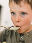 Nahaufnahme des entzückenden Jungen, der beim Mittagessen zu Hause appetitliche Sahnesuppe mit Löffel isst — Stockfoto