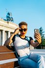 Mulher preta madura elegante em óculos de sol com lábios vermelhos e corte de cabelo moderno tomando auto-retrato no celular na cidade — Fotografia de Stock