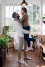 Smiling woman riding piggyback on boyfriend while looking at each other against windows at home — Stock Photo